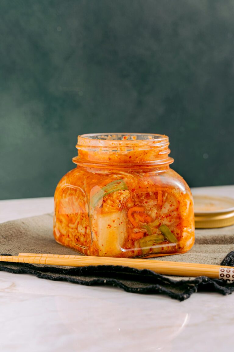Close-up of homemade kimchi in a jar with chopsticks on a table.